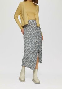 Yellow cardigan with buttons over a patterned midi skirt featuring blue and white flowers. The outfit is paired with light-colored ankle boots.