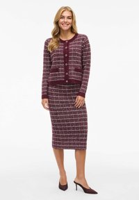 Cardigan en tricot bordeaux avec un motif vichy texturé, doté d'une fermeture à boutons et de deux poches. Jupe ajustée assortie dans un design similaire.