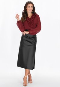 Bordó blúz fodros gallérral, hosszú áttetsző ujjakkal, fekete műbőr midiszoknya oldalsó hasítékkal; áttetsző sarkú szandállal párosítva.