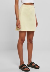Minifalda amarilla de algodón con cintura elástica, que presenta un ajuste relajado y una textura suave. Combinada con sandalias negras.