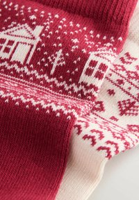 Strickstoff mit einem rot-weißen Farbschema, das ein winterliches Motiv zeigt. Enthält Schneeflocken, Bäume und geometrische Designs.