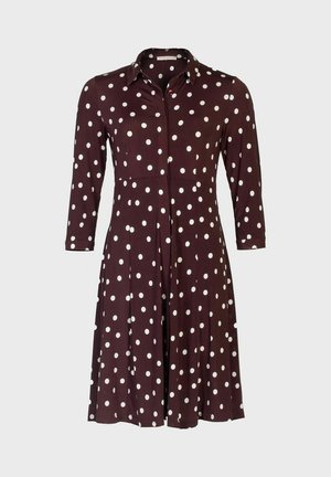 Bruine jurk tot op de knie met een knoopsluiting aan de voorkant en een kraag. Voorzien van witte polka dots, lange mouwen en een uitlopende rok.