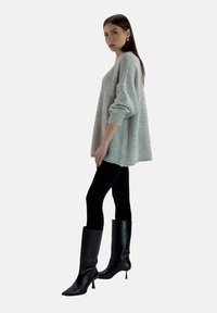 Suéter gris de gran tamaño de punto con puños acanalados, combinado con legging negros y botas de tacón alto negras hasta la rodilla. Diseño elegante y minimalista.