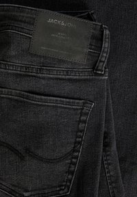 Svarta denimjeans med en strukturerad yta, försedd med en läderetikett märkta "JACK & JONES" och diskreta sömdetaljer.