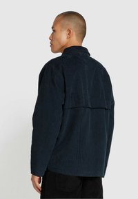 Veste en corduroy marine avec col, couture au dos tombé et texture côtelée, dotée de manches longues et d'une coupe décontractée.