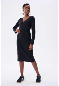 Schwarzes geripptes Langarmkleid mit V-Ausschnitt und taillierter Form, kombiniert mit schwarzen Sneakern mit weißen Streifen und Gummisohlen.