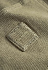 Beige stof med en firkantet syet lap, mærket "Lukket" med tråd i samme farve.