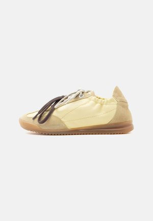 Scarpa da ginnastica casual beige e giallo chiaro con lacci a due tonalità e suola in gomma color caramello, mostrata di profilo su sfondo bianco.
