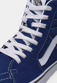 Μπλε ψηλό αθλητικό παπούτσι από σουέντ με λευκά κορδόνια και ρίγα στο πλάι, με ορατές ραφές και λογότυπο "Off The Wall" στη γλώσσα.