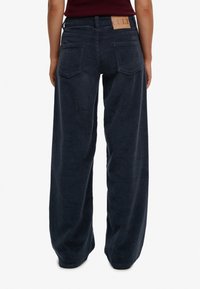 Granatowe szerokie spodnie sztruksowe o fakturowanym wykończeniu, z tylnymi kieszeniami i naszywką z logo ze skóry w kolorze jasnobrązowym na pasku.