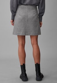Jupe en laine grise à coupe droite, de longueur mi-cuisse. Associée à des bottines noires, affichant un tissu texturé et des lignes épurées.