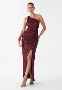 Ühe õlaga burgundi värvi litritega kleit drapeeritud disainiga ja reie kõrge lõhikuga. Sobitatud kuldsete aksessuaaride ja rihmikuga sandaalidega. Tekstureeritud kangas.