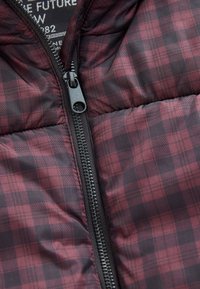 Veste matelassée bordeaux à motifs à carreaux, dotée d'une fermeture éclair en métal et d'une texture matelassée pour l'isolation.