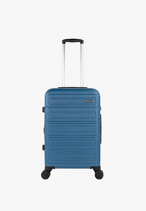 Maleta dura azul con ranuras, detalles en negro, asa extensible y cuatro ruedas para movilidad, con un logotipo en la parte delantera.