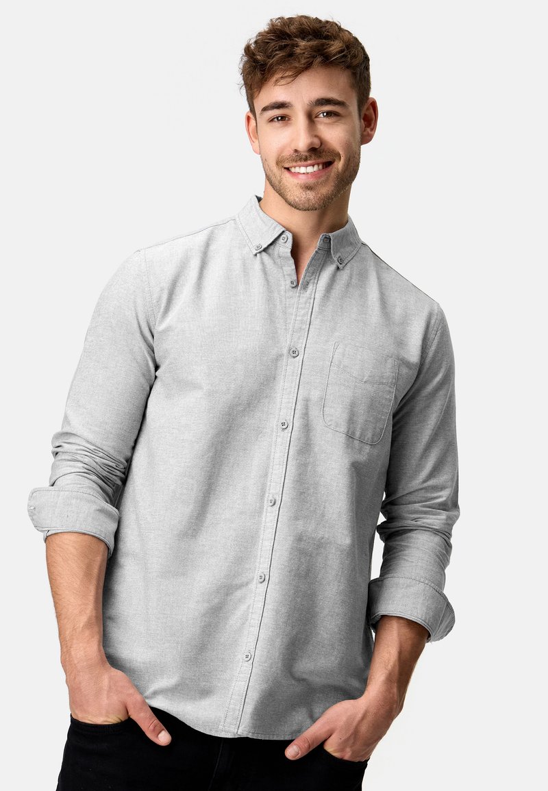 Camisa gris de botones con cuello, bolsillo en el pecho y mangas largas. La tela parece suave con una textura sutil.