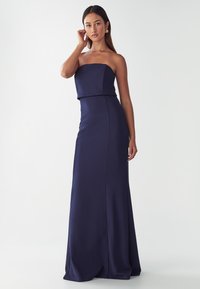 Jūras spēku strapless kleita, kas izgatavota no gludas auduma, ar pieguļošu krūšdaļu un plūstošu svārku, kas stiepjas līdz grīdai. Bez rakstiem vai rotājumiem.