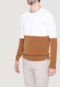 Maglione con una parte superiore bianca e una parte inferiore marrone. Realizzato in tessuto morbido, ha un collo rotondo e polsini aderenti.