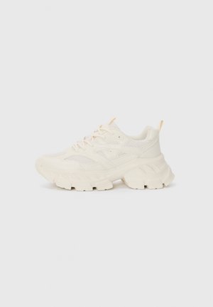 Chunky cream sneakers with mesh and synthetic panels, textured sole, round toe, and yellow accent at heel. Laces feature a slight sheen.
