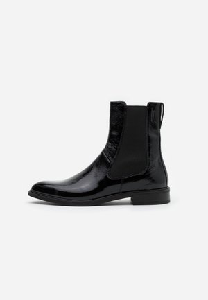 Skinnende sort læder Chelsea-støvle med elastisk sidepanel, trækflig og lav hæl, vist i sideprofil på hvid baggrund.