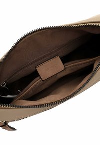 Interno di una borsa in pelle color tan con fodera in tessuto marrone, chiusura con zip e una piccola tasca con zip con un'etichetta in pelle impresso con la scritta "Tommy."