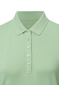Světlá zelená polo tričko vyrobené z texturované tkaniny, s límečkem a šesti odpovídajícími knoflíky podél légy.