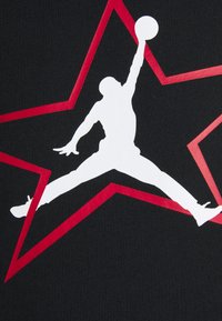 Tissu noir présentant une grande silhouette blanche d'un joueur de basket-ball en pleine plongée, sur fond d'une étoile rouge et de lignes géométriques.