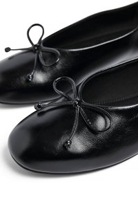 Bailarinas de cuero negro con puntera redondeada, adornadas con un lazo decorativo y una textura lisa y suave. Diseño clásico adecuado para un uso versátil.