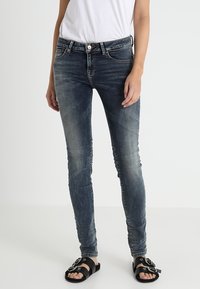 Slim-fit, středně vysoké džíny v tmavě modrém denimu s vybledlými akcenty; spárované s černými sandály se dvěma horizontálními pásky a kulatými přezkami.