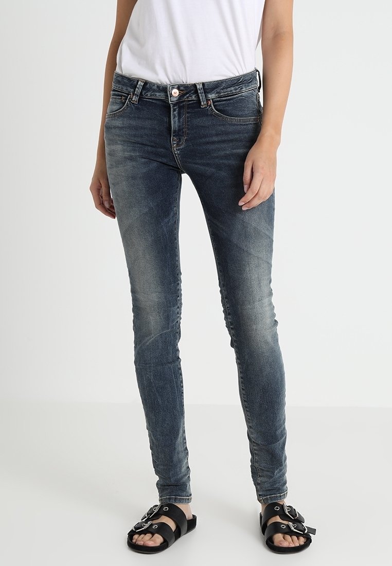 Slim-fit, středně vysoké džíny v tmavě modrém denimu s vybledlými akcenty; spárované s černými sandály se dvěma horizontálními pásky a kulatými přezkami.