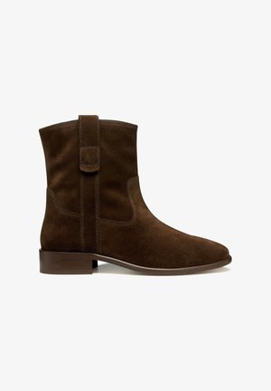 Stivaletto in suede marrone con tacco in legno basso, punta rotonda e maniglia laterale per un facile indossamento.