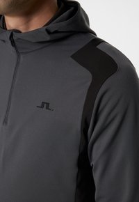 Grå dragkedjetröja med svart axelaccent och en liten logotyp. Tillverkad av ett mjukt tyg med en avslappnad passform och mjuk textur.