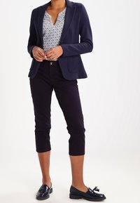 Námořnický blazer s kapsou, vzorovaný bílý a námořnický top, tmavé zkrácené kalhoty a lesklé černé mokasíny s mašlí.