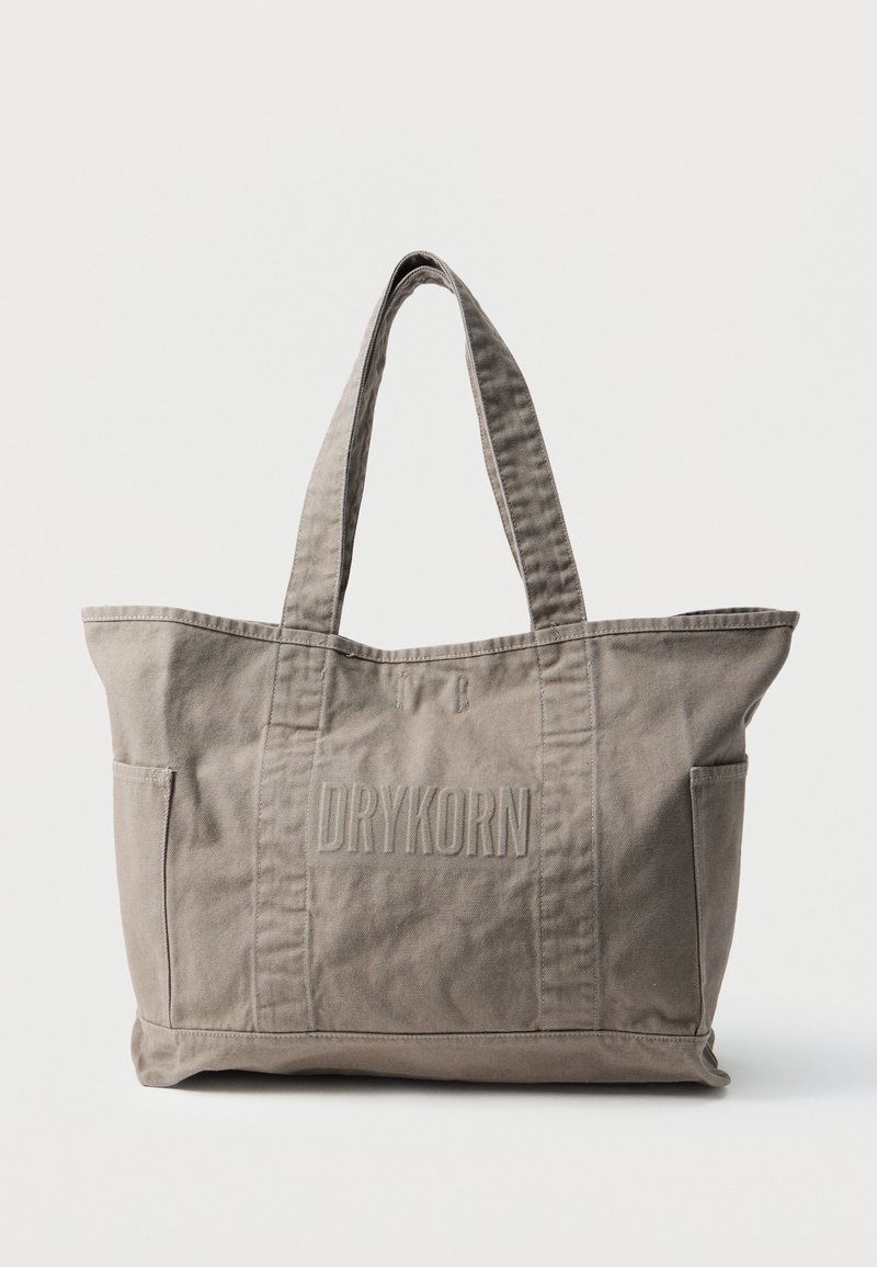 Borsa tote in tela color tortora con due manici, tasche laterali frontali e "DRYKORN" in rilievo al centro frontale.