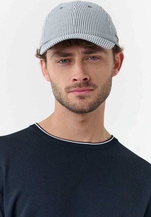 Young man with light beard wearing a striped gray and white cap and a dark navy sweater with a thin white trim on the collar.