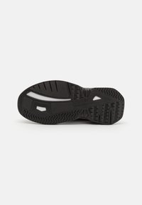 Suela de zapatilla negra con una superficie de goma texturizada, surcos prominentes y un panel con acentos blancos, diseñada para tracción y durabilidad.