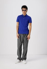 Camisa polo azul y pantalones grises. La camisa es de algodón con cuello y mangas cortas. Los pantalones son holgados con corte recto. Zapatillas blancas.