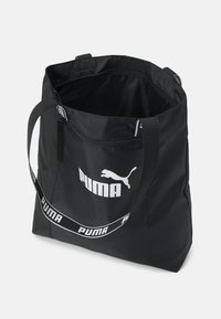 Zwarte nylon draagtasje met een voorste ritsvak, met een wit Puma-logo en een gebrandmerkte schouderriem. Van binnen heeft het een eenvoudig zwart voeringdesign.