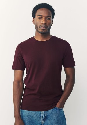 Bourgognefarvet t-shirt med korte ærmer lavet af blød bomuld, med en klassisk rund halsudskæring og en slank, tætsiddende pasform. Bæres med blå denimjeans.