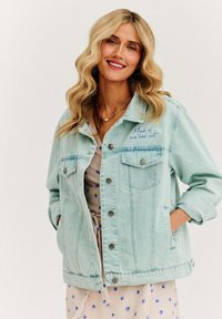 Jasnoniebieska kurtka dżinsowa z dwoma kieszeniami na piersi i srebrnymi guzikami. Zawiera haftowany napis "Zrobiona z słońca i soli." Casualowy, luźny krój.