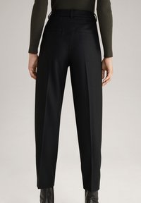 Pantalons noirs ajustés avec taille haute, plis et poches latérales, en tissu lisse. Une silhouette ajustée s'étend jusqu'à la cheville.
