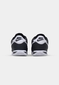Černé a šedé Nike tenisky s texturovaným povrchem, zdobené bílými akcenty a logem na patě, s kontrastním designem gumové podrážky.