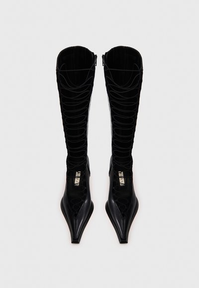 Μαύρες μπότες μέχρι το γόνατο με μυτερή μύτη, διαθέτουν σχέδιο με κορδόνια και υφασμένα πάνελ. Κατασκευασμένες από λείο δέρμα με γυαλιστερό φινίρισμα.