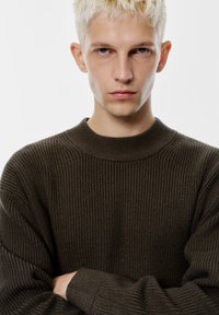 Pulover texturat de un verde închis, cu guler rotund și mâneci lungi, având detalii ribbate și un aspect moale, cald.