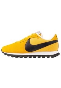 Nike sneakers med övre del i gul mocka, svart läder-swoosh, vit mellansula och svart gummiyttersula med spikar för grepp.