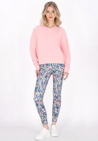Felpa oversized rosa chiaro con scollo a V abbinata a leggings aderenti a motivo blu, rosa e crema con una finitura lucida.