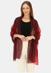 Przezroczysty burgundowy szal o lekkim, zwiewnym fasonie; noszony rozpięty, z miękkimi krawędziami i luźnym krojem. Połączony z czarną bluzką i jasnymi spodniami.