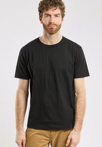 T-shirt en coton noir avec des manches courtes, un col rond et une texture lisse. Design simple, sans graphiques ni logos.