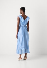 Light blue midi dress with ruffled sleeves and a tied waist. Flowing fabric features a layered hem. Worn with beige slingback heels.