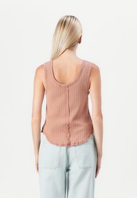 Lichtroze geribbelde tanktop met ronde halslijn en een gegolfde zoom, met een centrale naad en mouwloos ontwerp. Gedragen met lichtblauwe jeans.