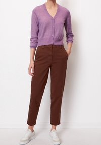 Lila V-ringad cardigan med knäppning, bärs över bruna raka byxor. Vita sneakers fulländar looken.